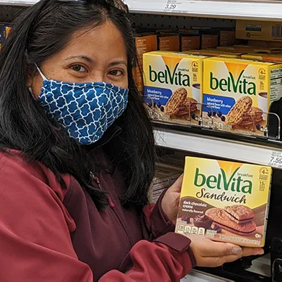 A publisher in a grocery aisle holding boxes of belVita breakfast sandwiches