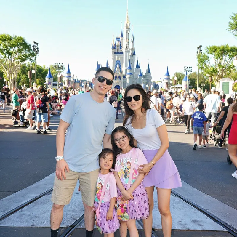 A family of four in front of Cinderella Castle at Magic Kingdom, the girls in Disney princess shirts