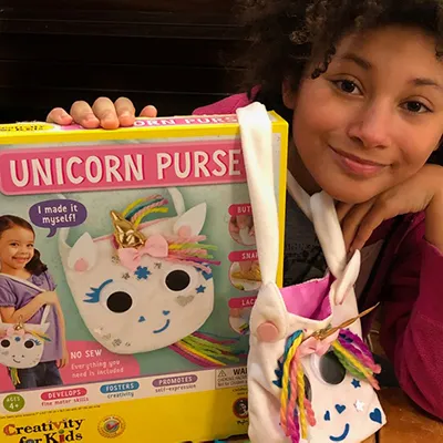 A girl with a Creativity for Kids unicorn purse craft kit and the purse she made
