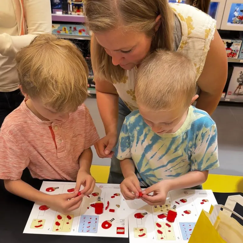 Two boys building with LEGO bricks from an instruction sheet while a parent helps at a LEGO store