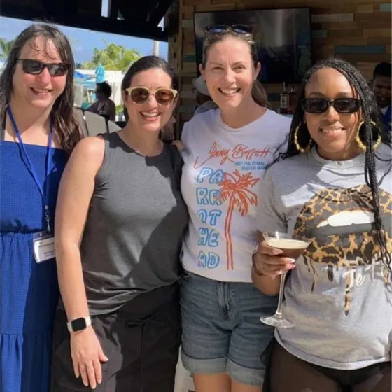 Four Macaroni KID publishers smiling together at a poolside bar
